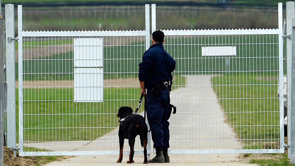 Ein Wachmann mit Hund steht vor einem Zaun bei Agroscope in Reckenholz-Tänikon.