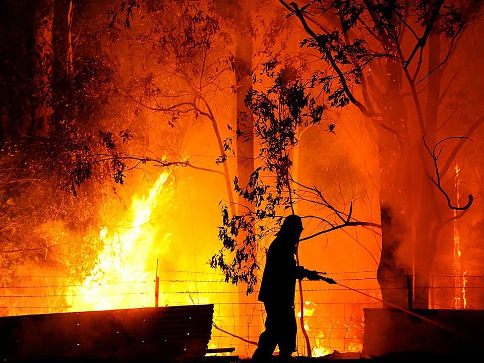 Ein einsamer Feuerwehrmann in Wandandian spritzt einen dünnen Wasserstrahl in die Flammen.