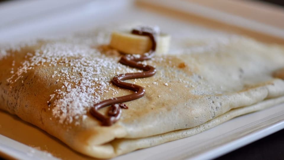 Eine schön gefaltete Crèpe auf einem Teller mit Schokolade und Puderzuckerdeko.