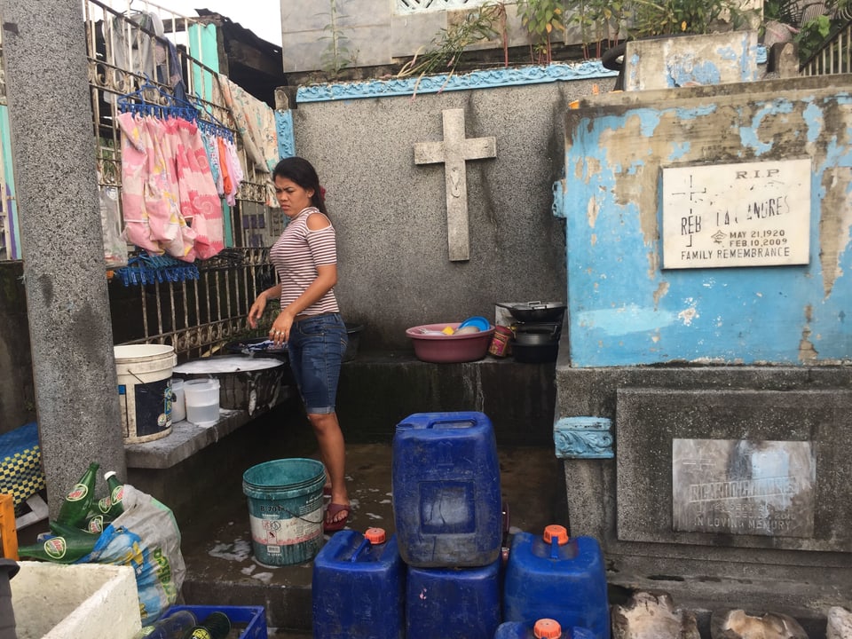 Eine junge Frau wäscht draussen zwischen einem Mausoleum und der Friedhofsmauer ihre Wäsche.