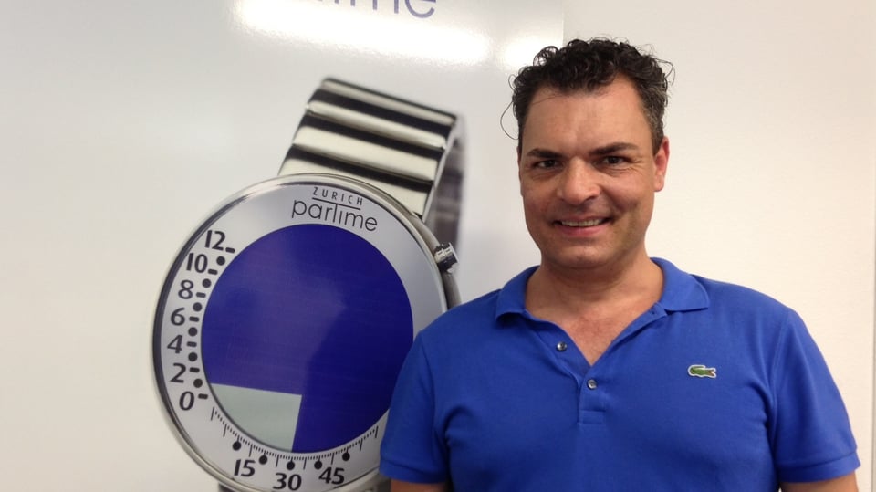 Andreas Mossner, der Erfinder der Züri-Uhr vor einem Plakat mit seiner Erfindung.