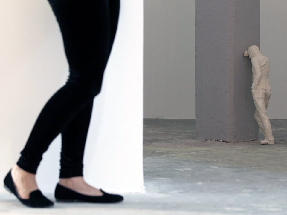 Dei Beine einer Frau stehen vor einer Skulptur, die an einem Pfeiler lehnt.