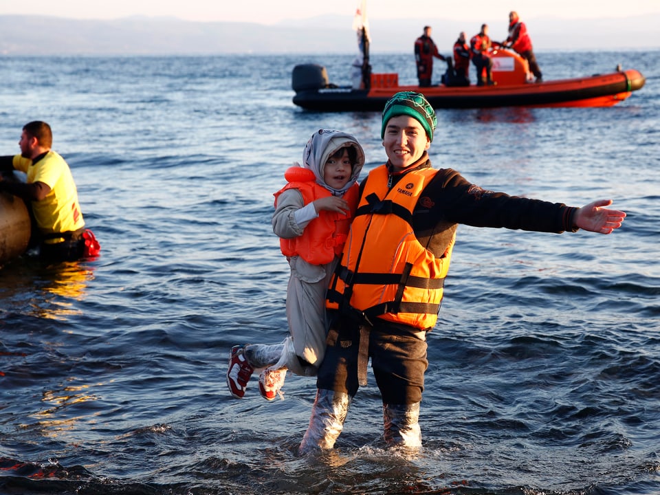 Ein junger Mann freut sich sichtlich, Lesbos erreicht zu haben, er hält ein Kind im Arm.