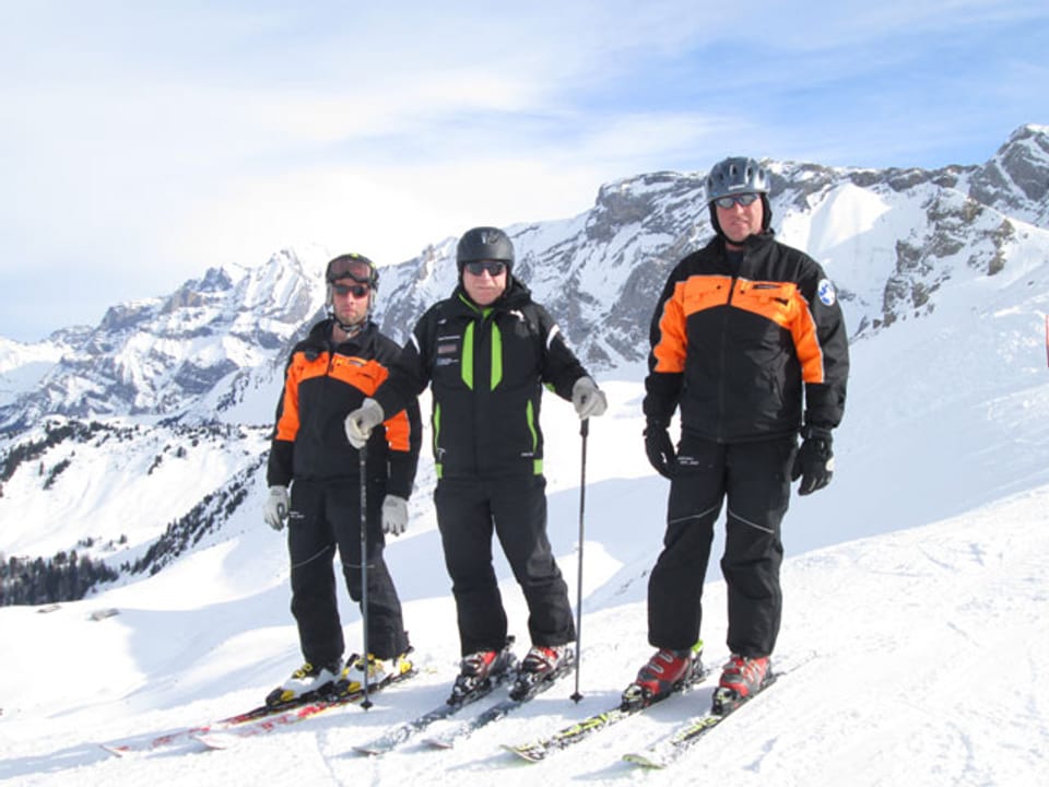 Drei Männer mit Skiausrüstung auf einer Skipiste.