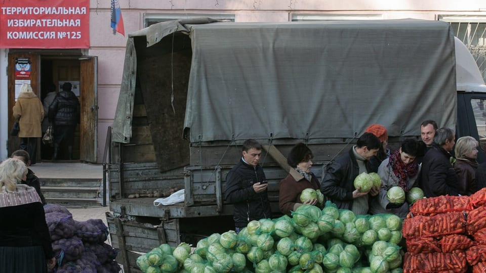 Menschen bei Gemüsekörben hinter einem Armee-Lastwagen