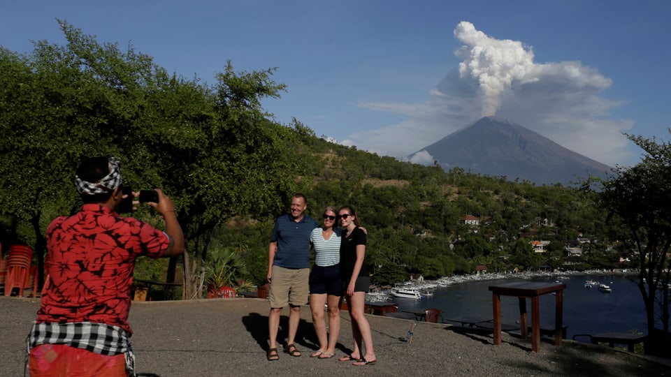 Touristen posieren vor Vulkan. Guide schiesst ein Foto.