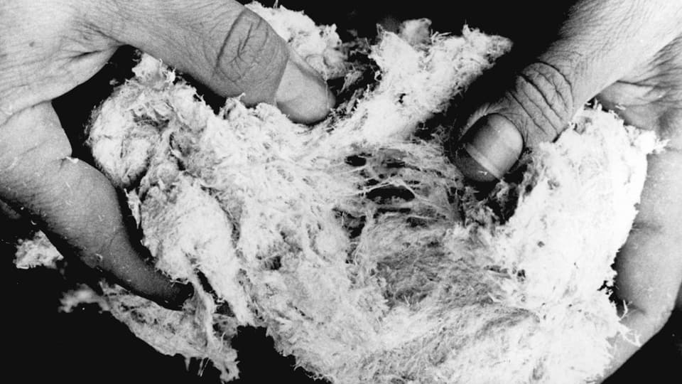 Schwarzweissfoto von zwei Händen, die einen ballen Asbest halten.