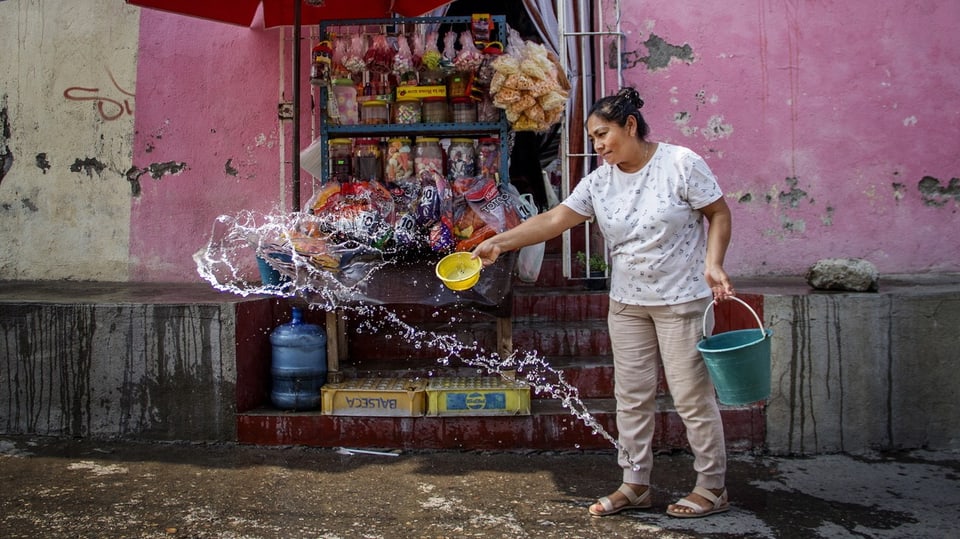 Eine Frau in Mexiko verteilt Wasser auf dem Boden, um die Auswirkungen der Hitze zu mildern.