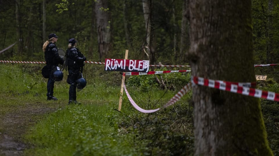 Zwei Polizistinnen stehen in Vollmontur im Wald neben einem Schild mit der Aufschrift: «Rümi bleibt».