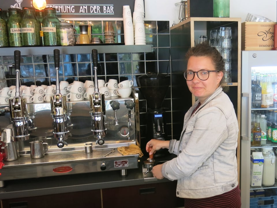 Eine Frau steht vor einer kaffemaschine und bedient sie. 