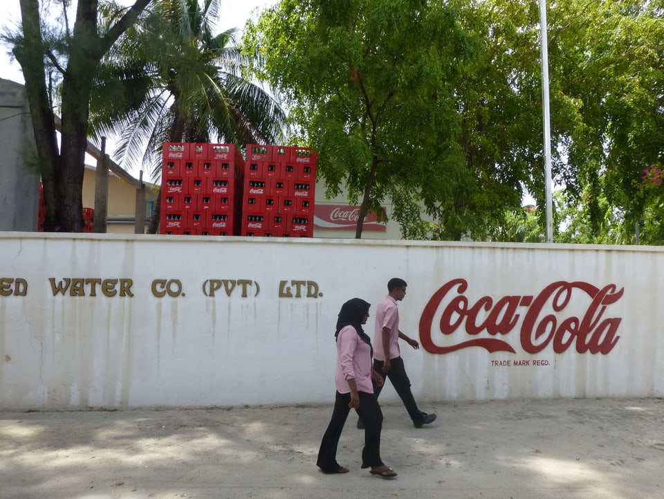 Zwei Arbeiter gehen an der Coca Cola Fabrik vorbei.