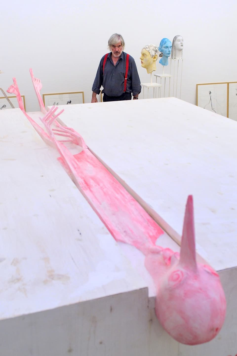 Der Künstler neben einer liegenden, rosaroten Skulptur, die einen dünnen Menschen darstellt.