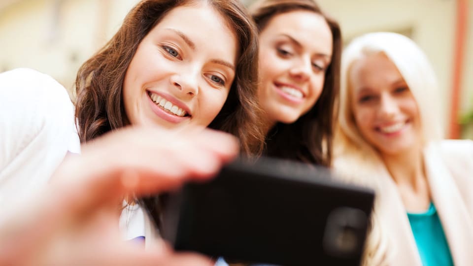 Drei junge Frauen schauen lachend auf ein Smartphone