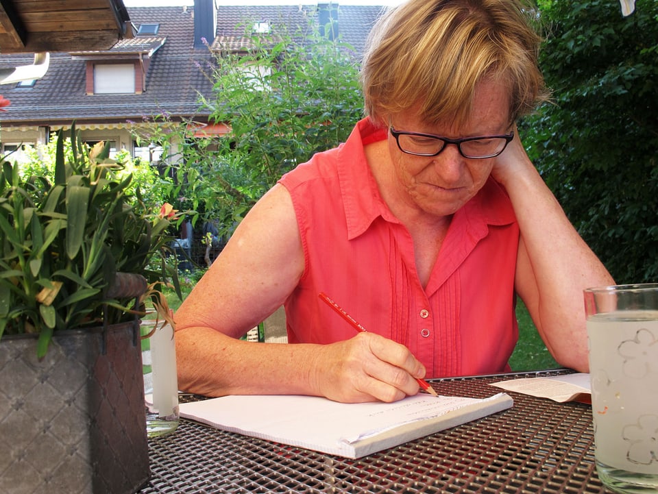 Ursula Diener sitzt am Gartentisch und schreibt.