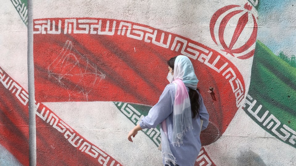 Frau vor einem Wandbild mit iranischer Flagge.