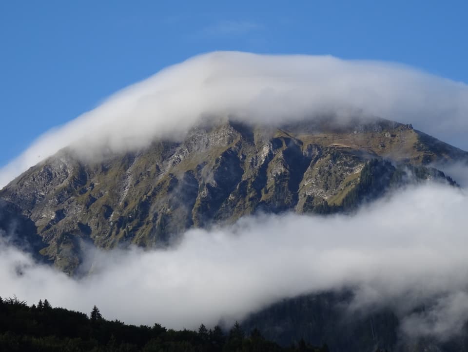 Berg, an welchem unten ein Nebelband hängt und der Gipfel in einer Nebelkappe hat.