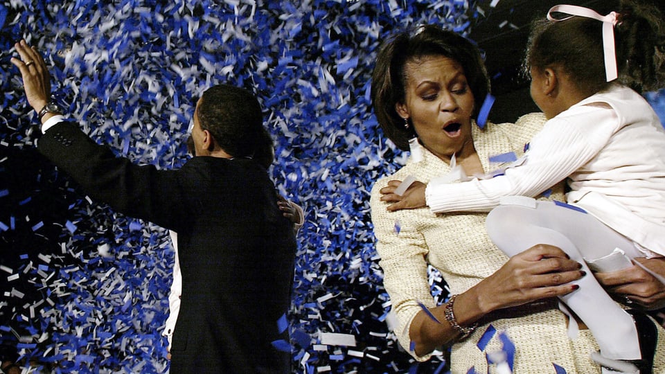 Barack Obama von hinten winkend. Michelle Obama im Vordergrund ihre Tochter tragend.