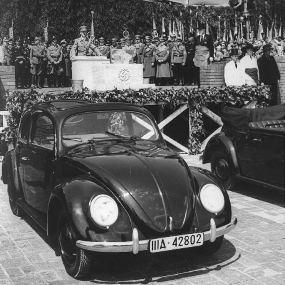 Adolf Hitler hält eine Rede. Vorne steht ein VW Käfer.