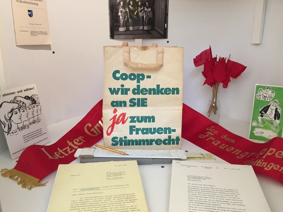Ausstellungsstücke zum Thema Frauenstimmrecht in der Schweiz in einer Auslage.