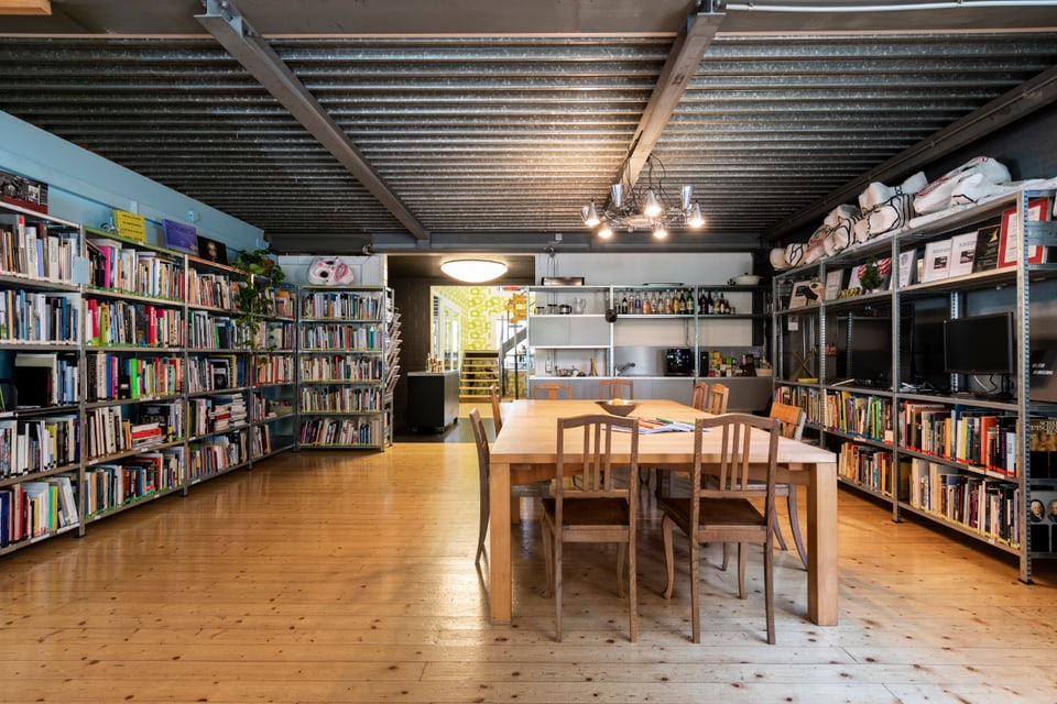 Grosser farbiger Raum mit Büchergestell und Tisch in der Mitte. 