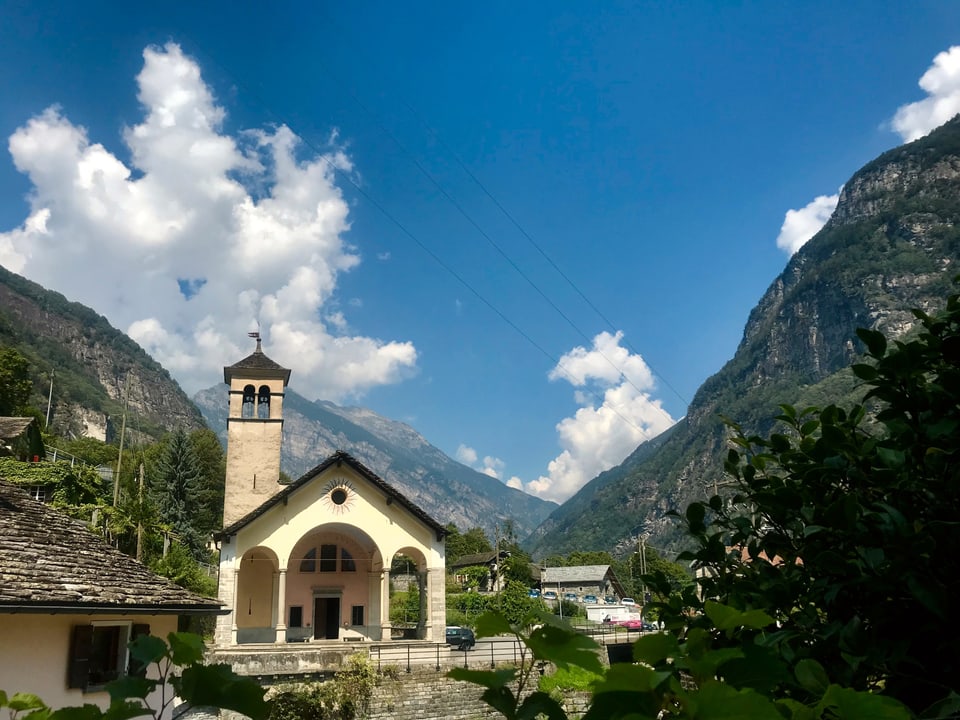 Die Kirche von Cevio zwischen den Tessiner Bergen, darüber Quellwolken.
