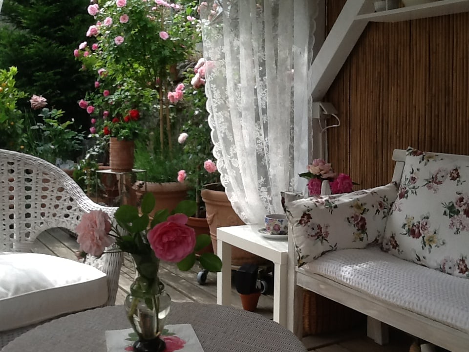 Ein Sitzplatz draussen mit schönen weissen Möbeln und rosa roten Rosen