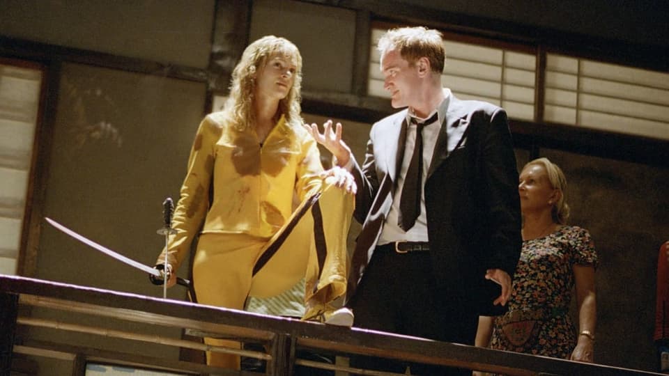 Ein Regisseur steht beim Dreh neben einer Schauspielerin mit einem Schwert in der Hand.