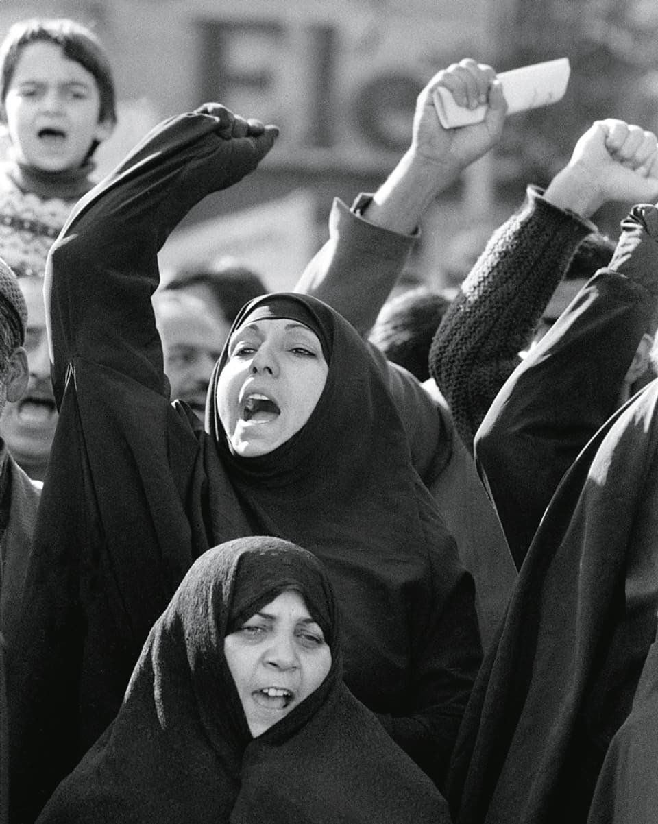 Iranische Frauen im Tschador demonstrieren mit erhobenen Fäusten.