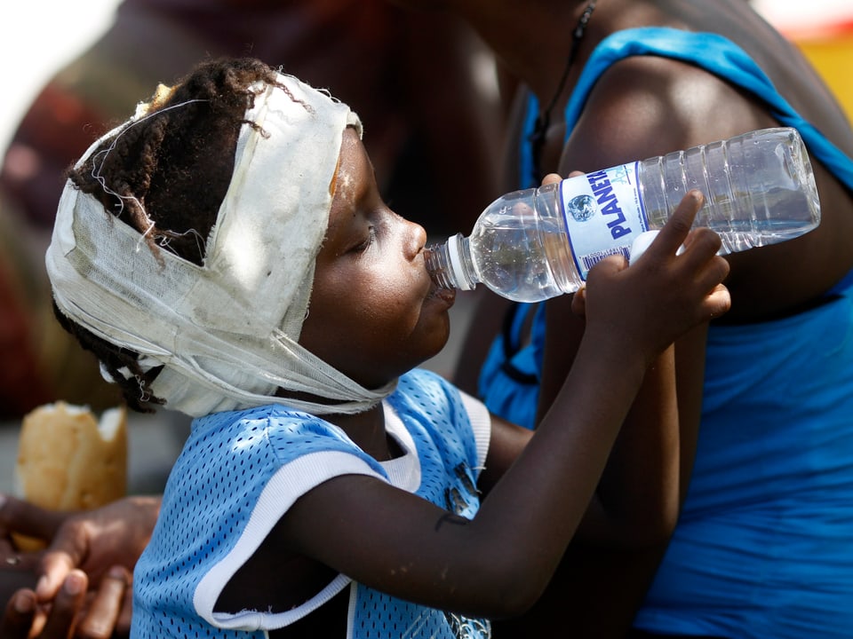 Ein Kind mit bandagiertem Kopf trinkt aus einer Wasserflasche