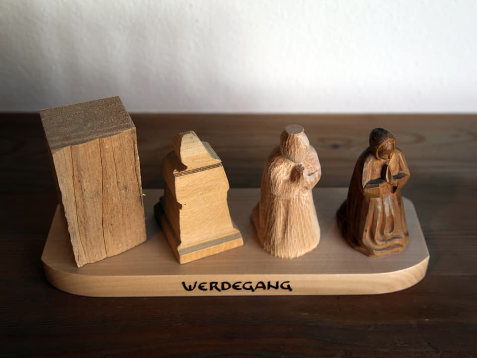 Das Bild zeigt den Prozess von einem Stück Holz in vier Schritten, wie es die Form einer Figur annimmt. 