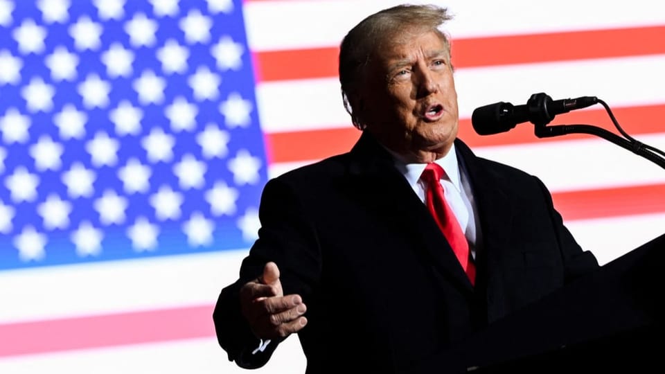 Mann in dunklem Anzug und roter Krawatte steht an Rednerpult. Im Hintergrund die US-Flagge.