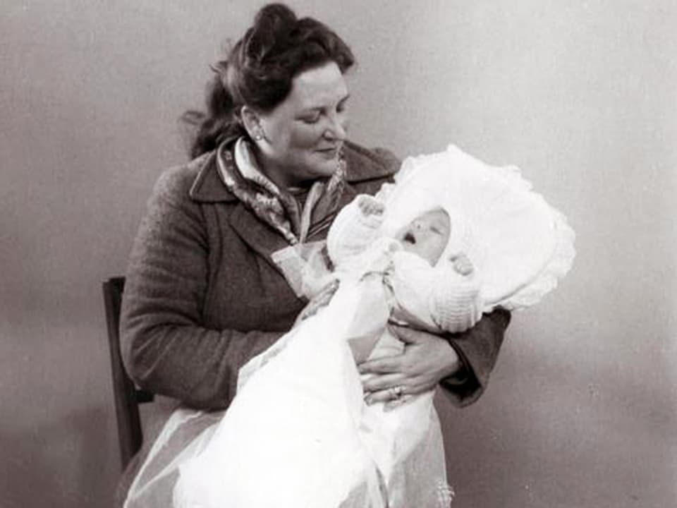 Frau mit Baby in Taufkleidung auf dem Arm.