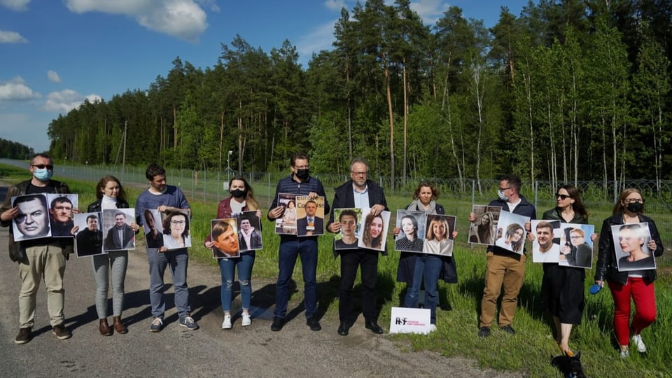 Zehn Menschen halten A3-Fotos von festgenommenen Journalistinnen und Journalisten in den Händen.