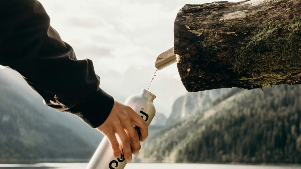 eine Flasche wird an einem Brunnen mit Wasser aufgefüllt