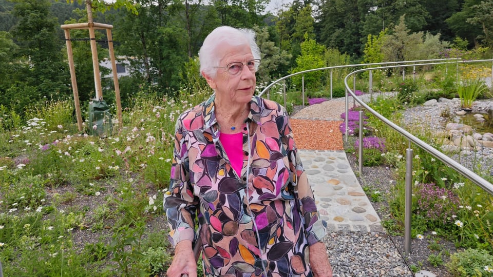 Ältere Dame in blumigem Kleid in einem Garten.