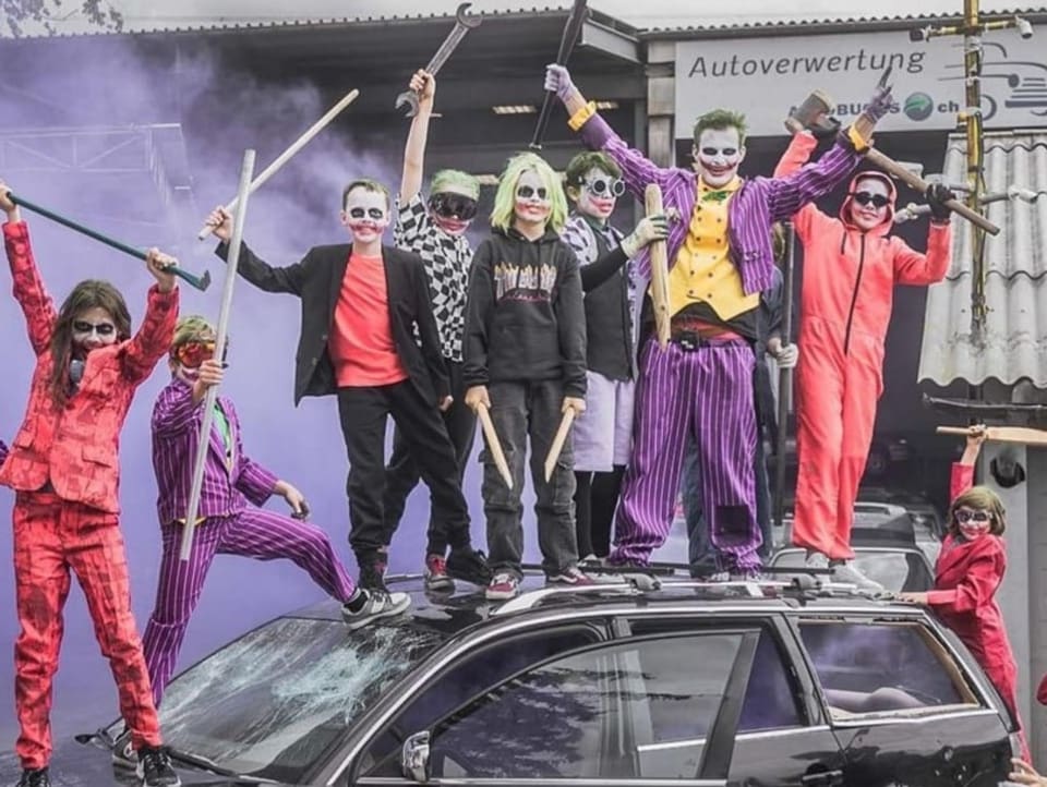 Nicolas Huber und verkleidetet Kinder stehen mit Baseball-Schlägern auf einem Auto. 