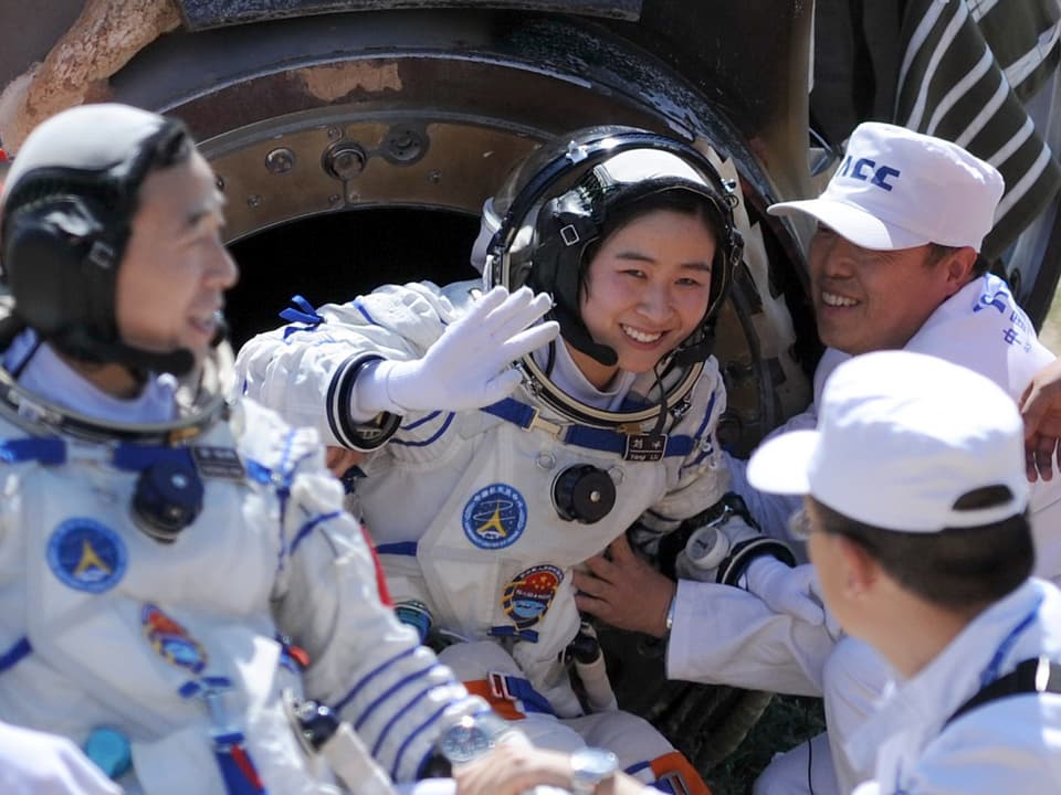Die Astronauten besteigen mithilfe zweier Männer die Raumkapsel und winken.