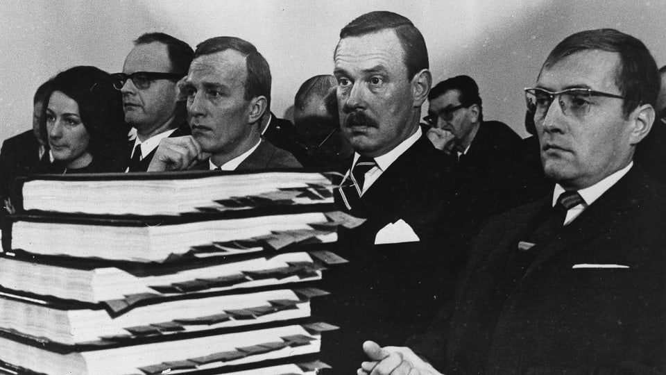 Schwarz-weiss-Foto: Männer hinter einem Stapel Bücher.