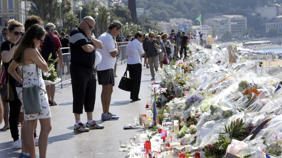 Menschen betrachten Trauerbotschaften und Blumen an der Promenade des Anglais in Nizza nach dem Attentat.