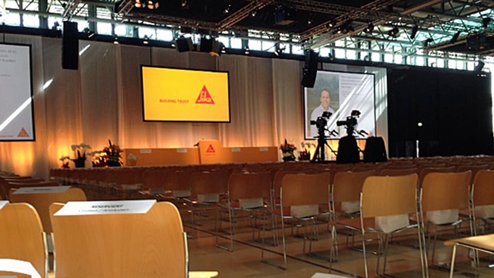 Der noch leere Saal in Baar mit Blick auf das Podium, im Vordergrund ein Schild "Reserviert für Medien/Analysten"