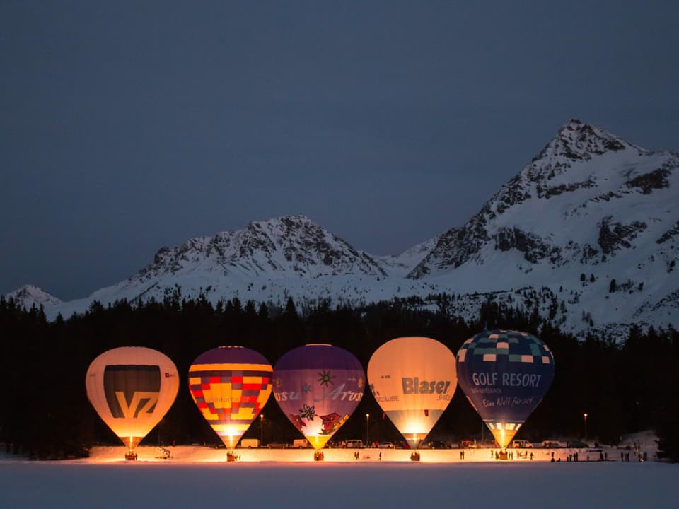 Feuernde Ballone stehen am Boden in verschneiter Landschaft. 
