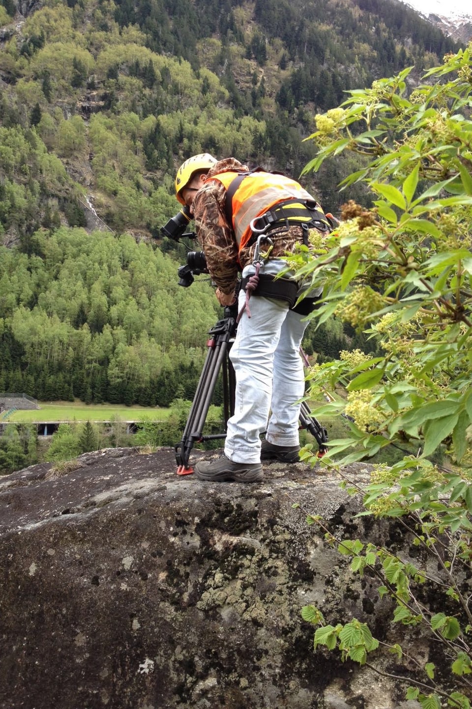 Kameramann steht auf einem Felsbrocken und richtet die Kamera vor sich hinunter in die Tiefe.