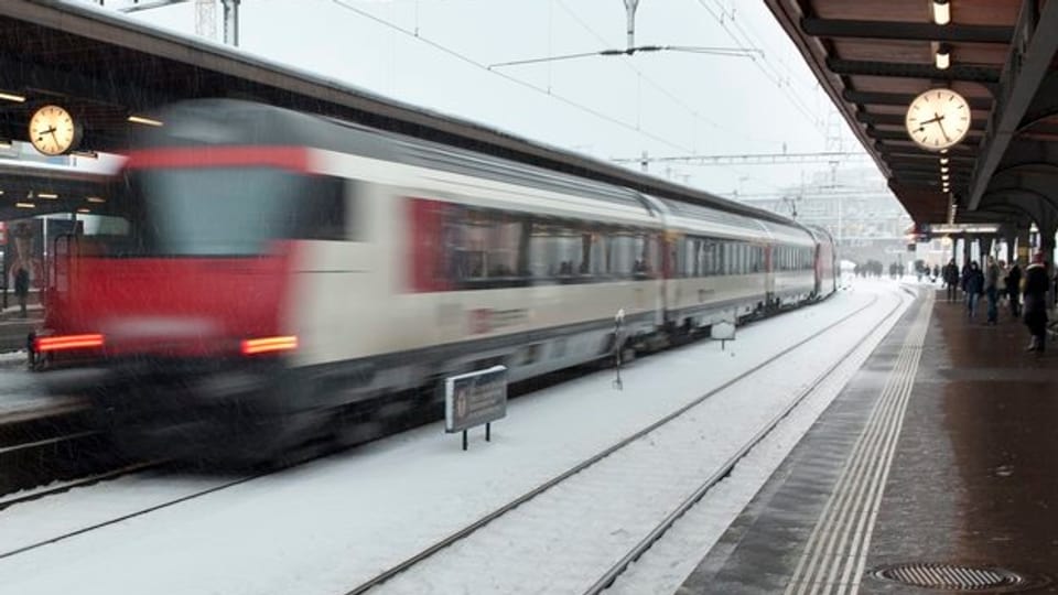 Ein Interregio-Zug flitzt durch einen Bahnhof, es hat Schnee auf den Geleisen.