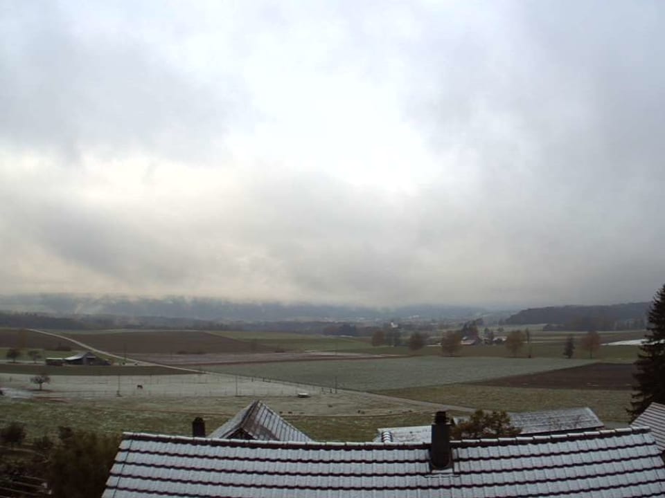 Felder, im Vordergrund Dächer mit wenig Schnee