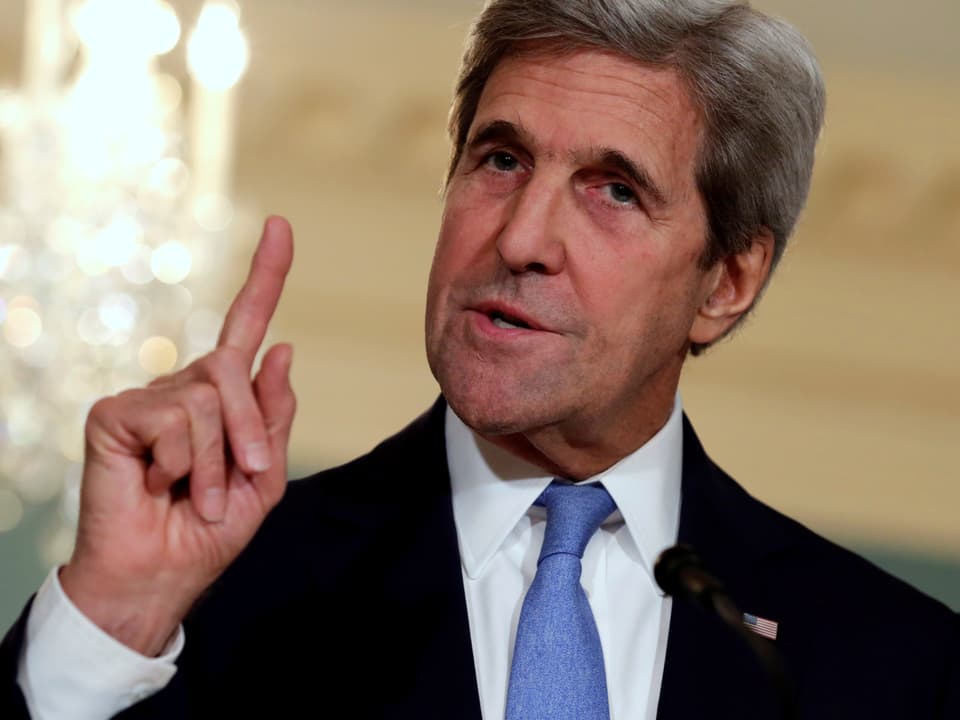 John Kerry spricht an einer Medienkonferenz und hält den Zeigefinger mahnend hoch. 