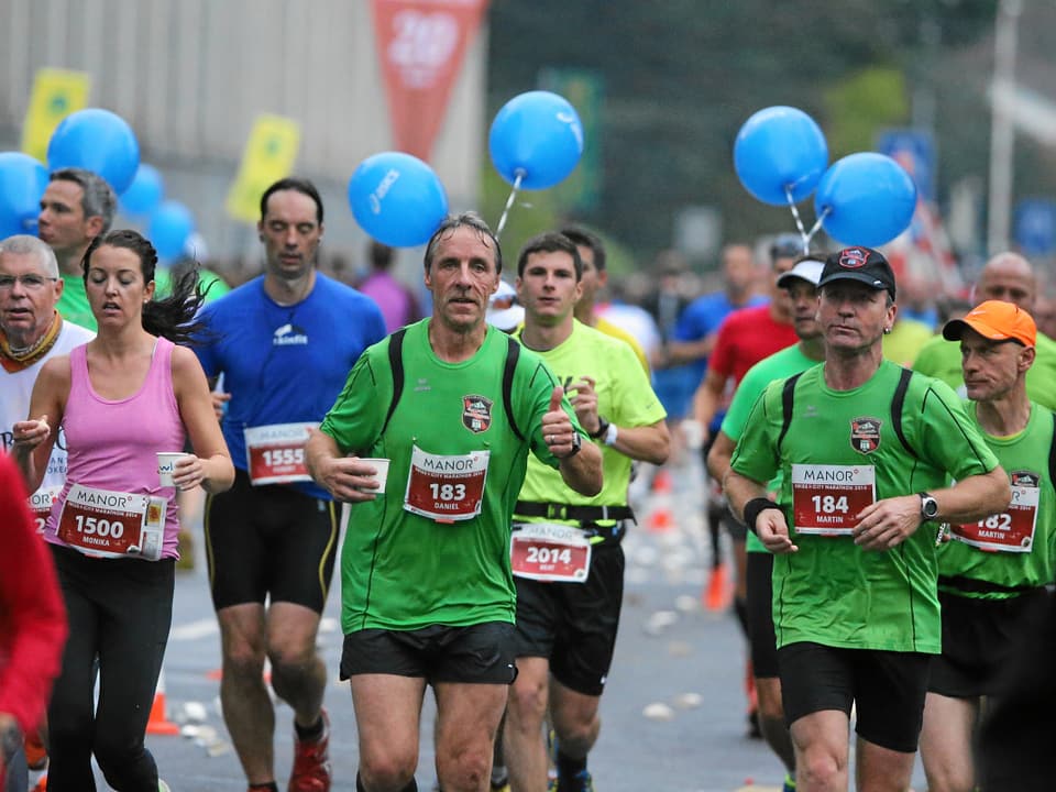 Männer in grünen Sporshirts laufen einen Marathon.