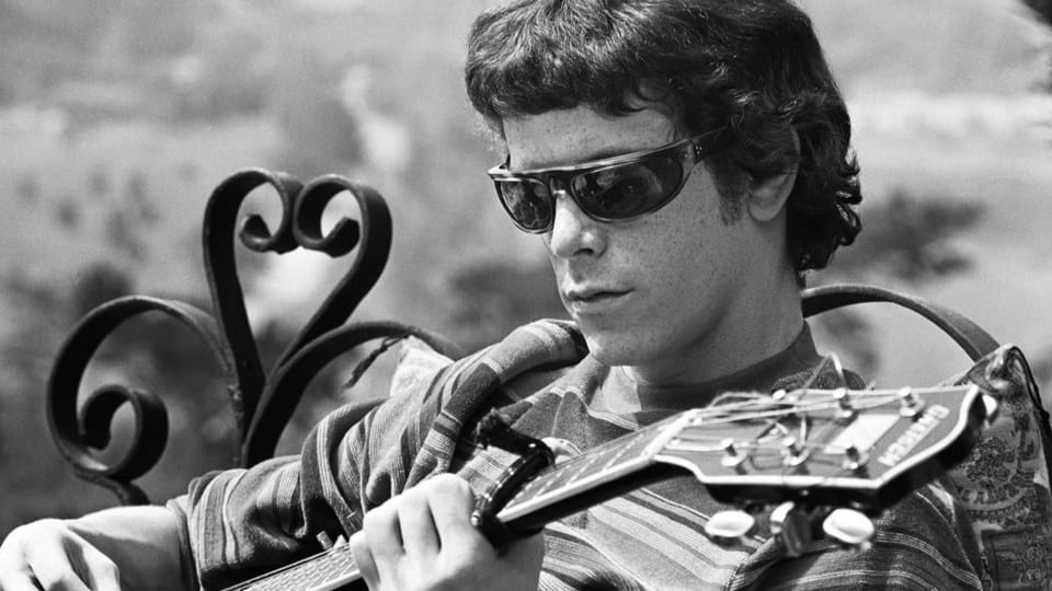 Schwarzweiss-Nahaufnahme von Lou Reed mit Sonnenbrille und Gitarre.