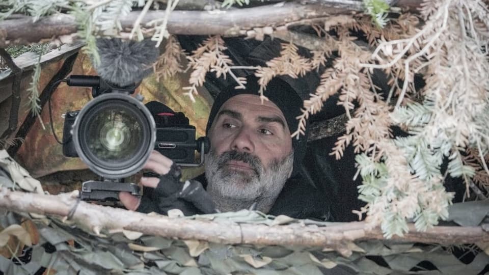 Ein Mann sitzt mit einer Kamera in einer selbstgebauten Hütte.