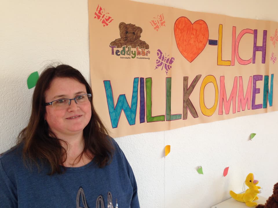 Chefin Sonja Hümbeli steht vor einem Herzlich Wilkommen Plakat