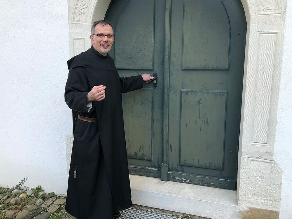 Ein Mönch vor einer grossen Holztüre.